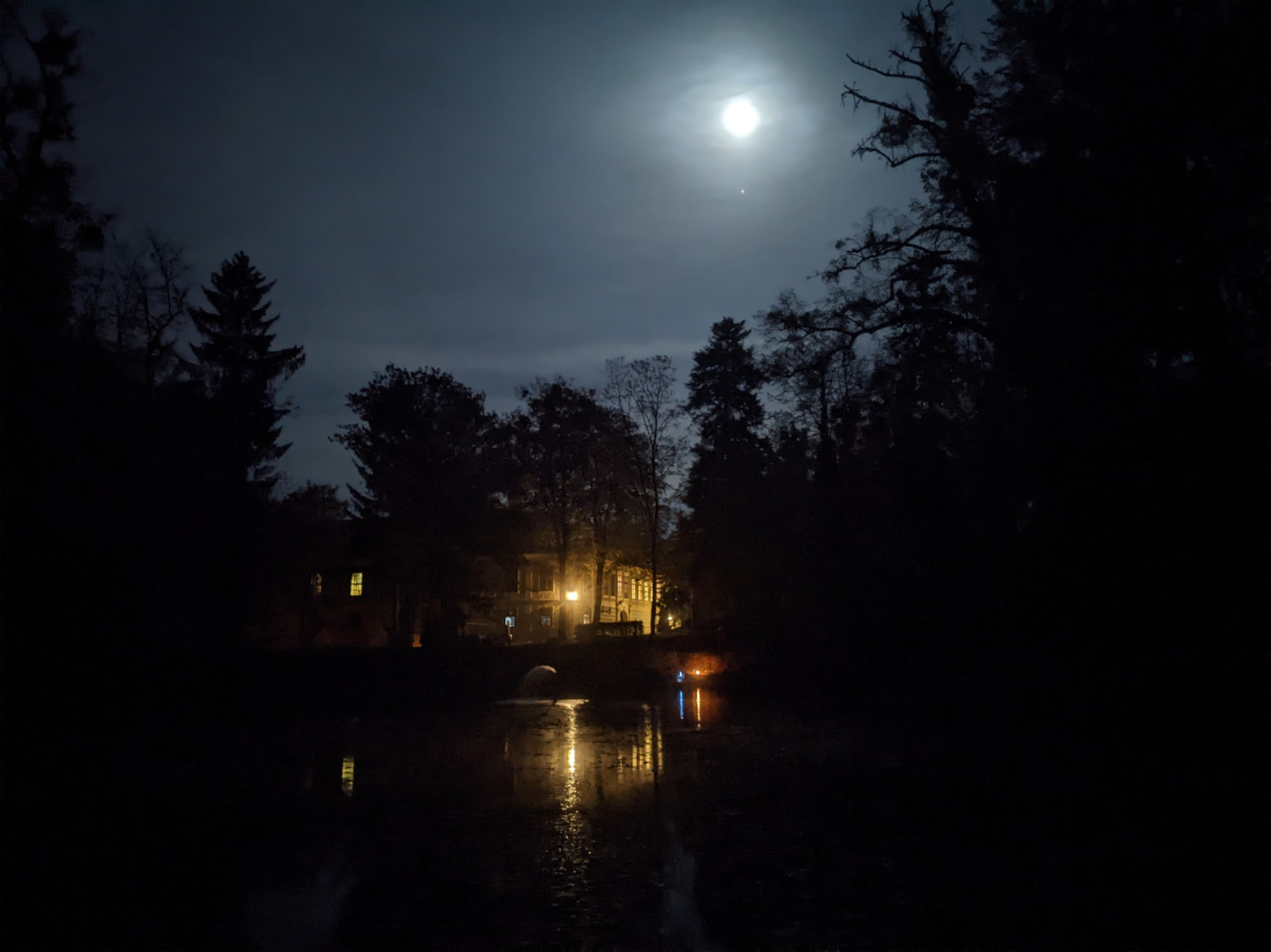 Hostačov at night, the house lights and moon reflected in the lake
